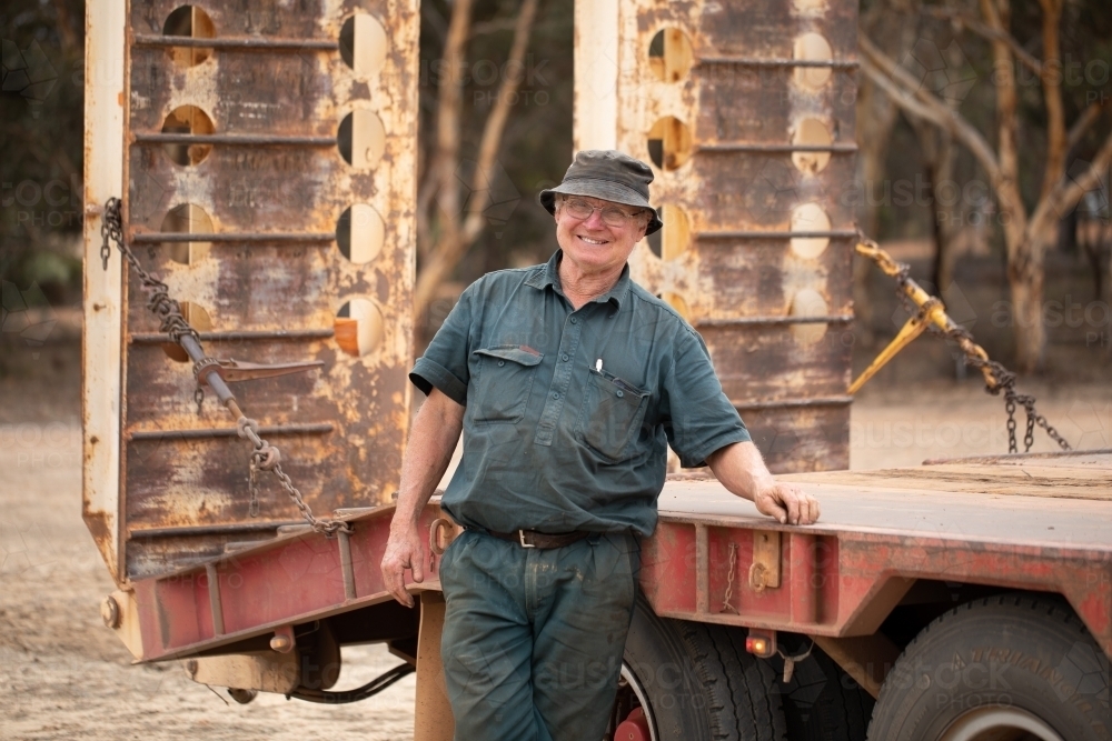 older man smiling and leaning on truck tray - Australian Stock Image