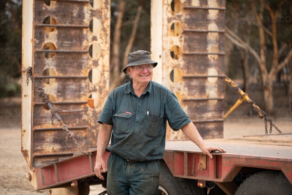 older man smiling and leaning on truck tray - Australian Stock Image