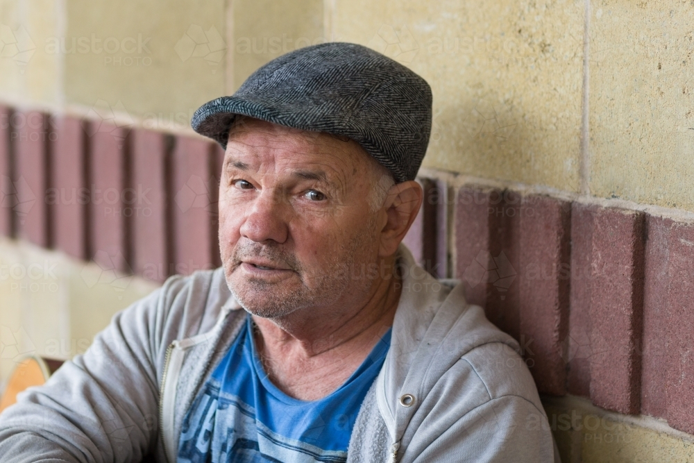 Older man wearing Yorkshire cap leaning on concrete wall - Australian Stock Image
