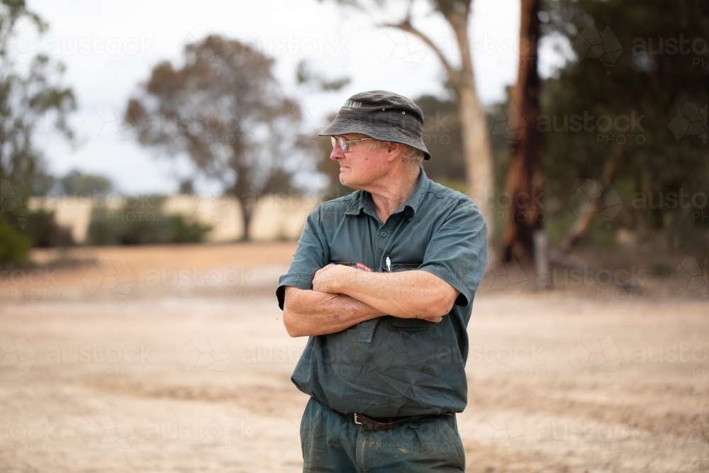 older man with grim look on his face and arms folded looking away - Australian Stock Image