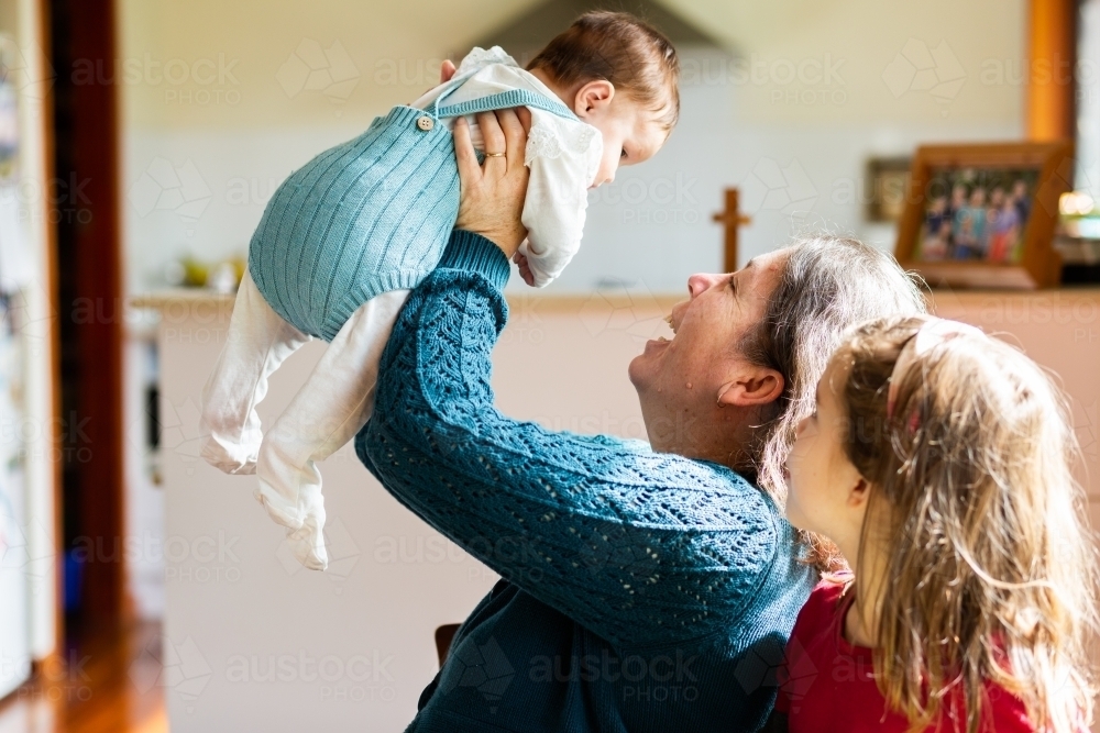 Older mum playing with two daughters inside home - Australian Stock Image