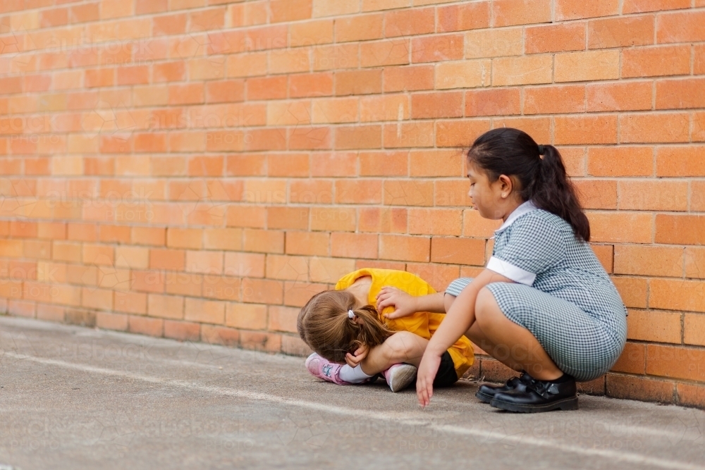 Older school girl comforting younger child who got bullied by classmates - Australian Stock Image