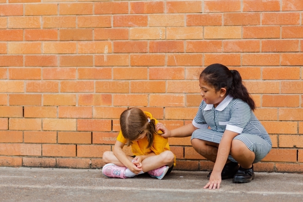 Older school girl comforting younger child who got bullied by classmates - Australian Stock Image