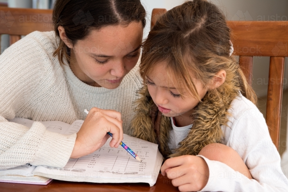Older sister helping younger sister with school homework. - Australian Stock Image