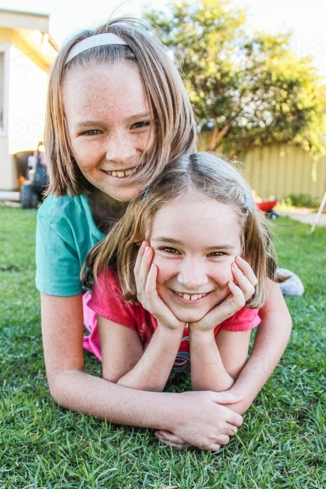 Older sister lying on top of younger sister happy smiling - Australian Stock Image