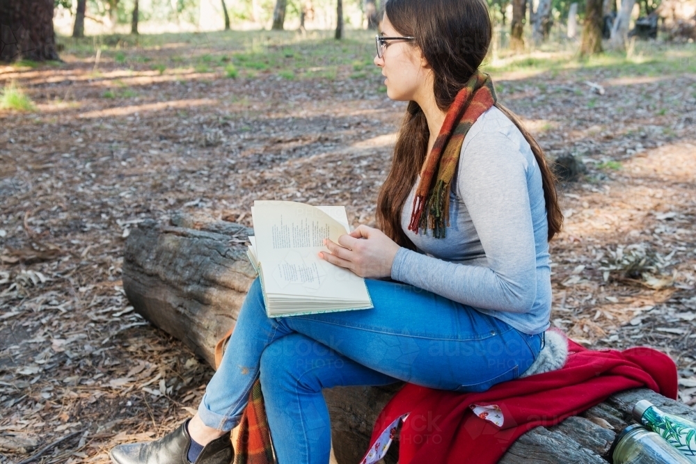 Image of older teen girl reading a book in the forest - Austockphoto