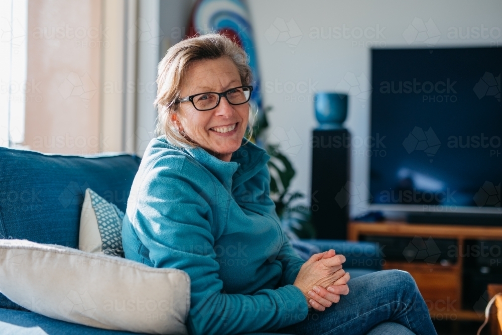 Older woman looking happy smiling in lounge room - Australian Stock Image