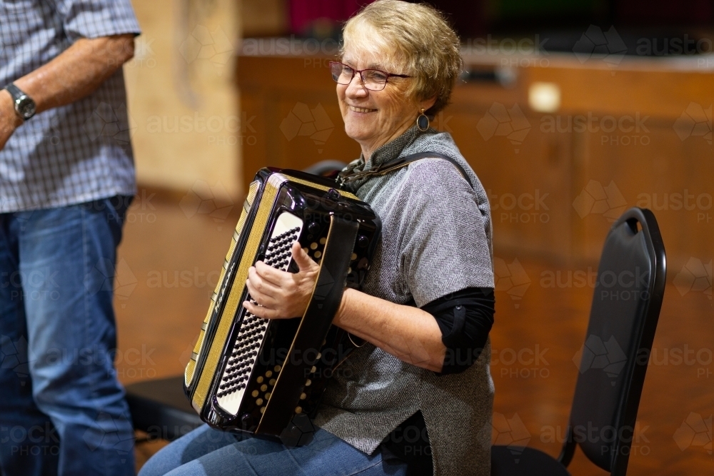 older woman seated playing accordion - Australian Stock Image