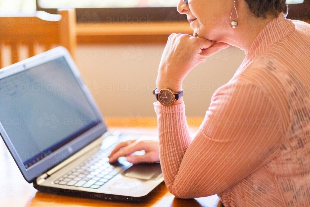 Image of Older woman using laptop computer at dining table - Austockphoto