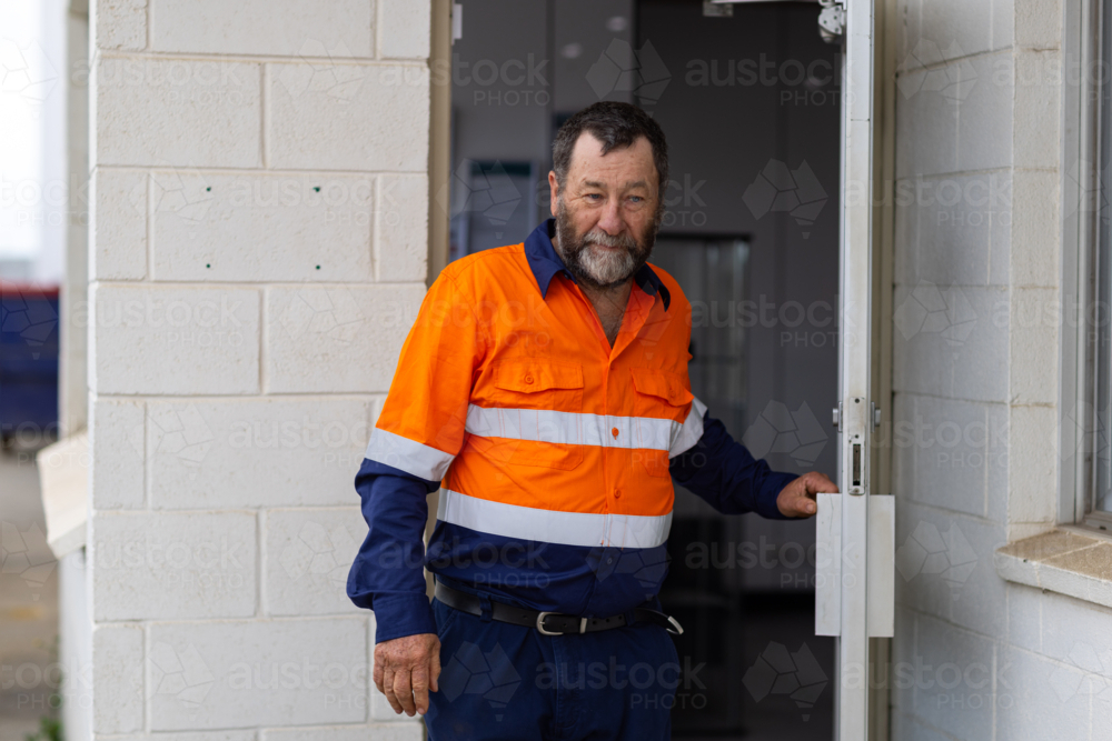 Older working class man coming out of the offices glass door - Australian Stock Image