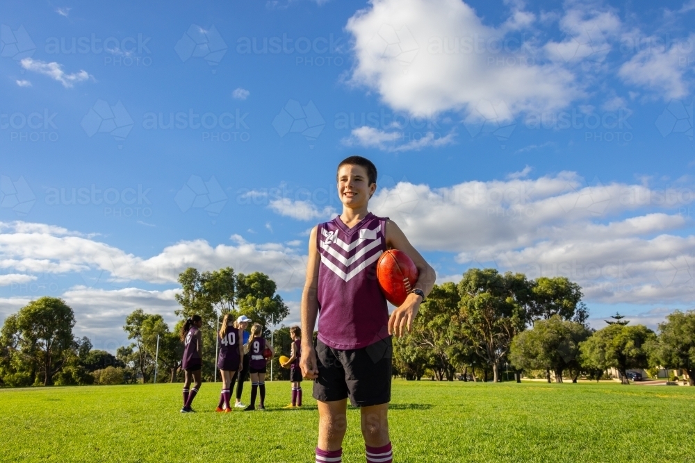 one boy in football uniform standing in front of his teammates holding a football - Australian Stock Image