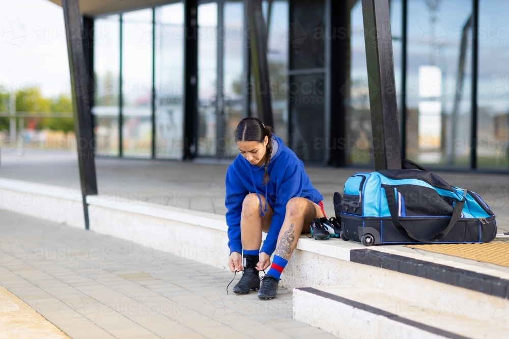 one female football player sitting on clubhouse step tying bootlaces - Australian Stock Image
