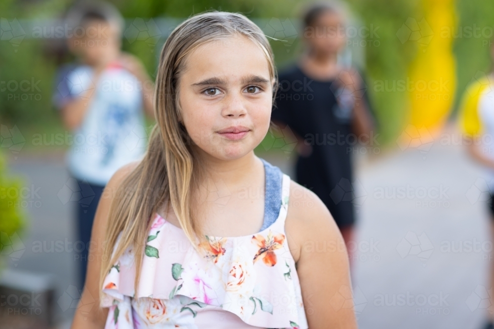 one girl looking at the camera with other children blurred in background - Australian Stock Image