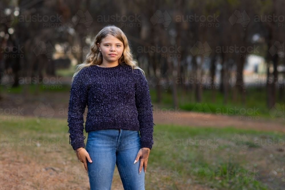 one girl wearing jeans and jumper standing outdoors by herself - Australian Stock Image