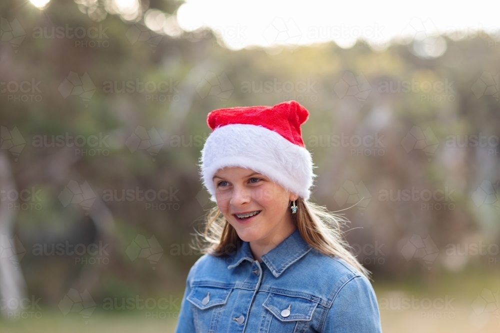 one girl with braces on her teeth wearing christmas hat outdoors with burry background - Australian Stock Image