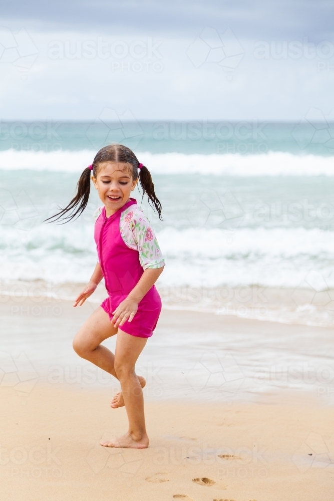 One happy little girl in pink playing and running in sand by the seaside - Australian Stock Image