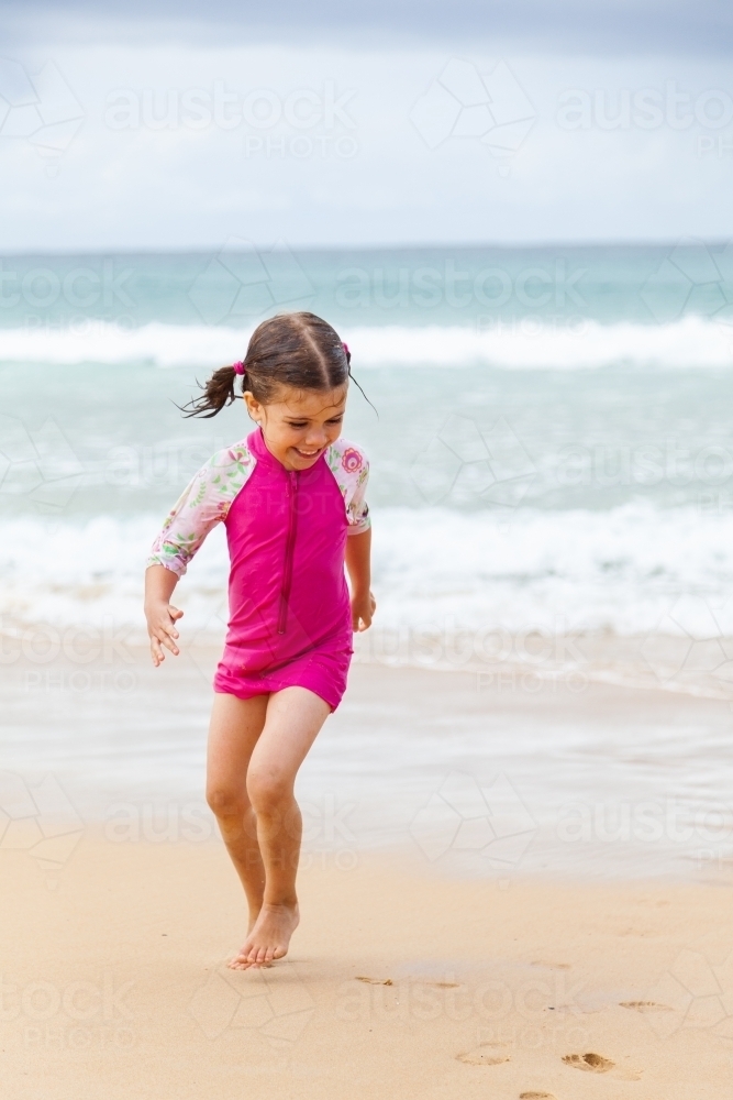 One happy little girl in pink playing and running in sand by the seaside - Australian Stock Image