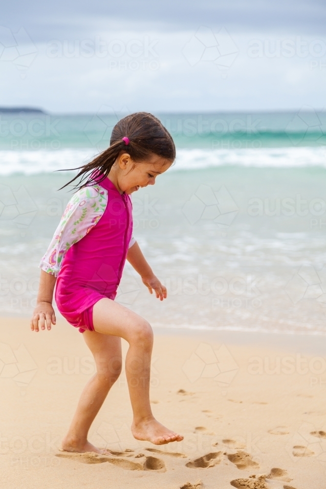 One happy little girl in pink playing and running in sand by the seaside - Australian Stock Image