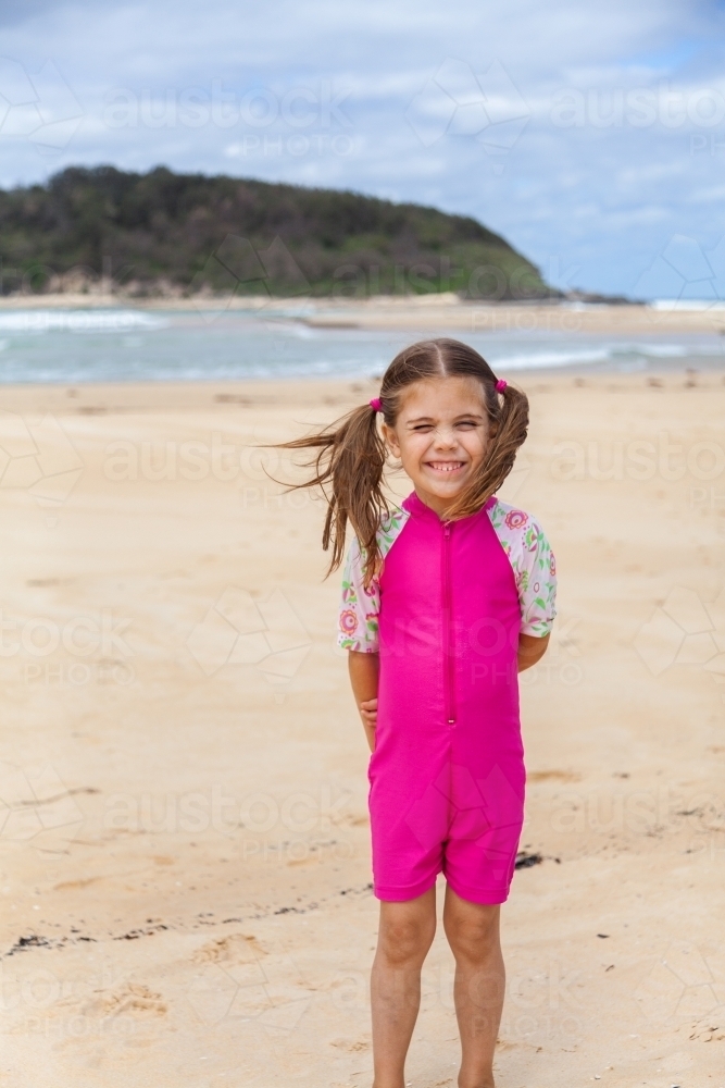 Image of One happy little girl in pink standing in sand by the seaside ...
