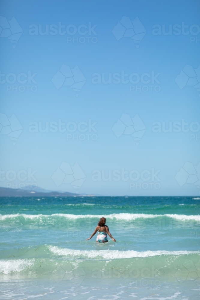 one person wading out into the waves at the beach - Australian Stock Image
