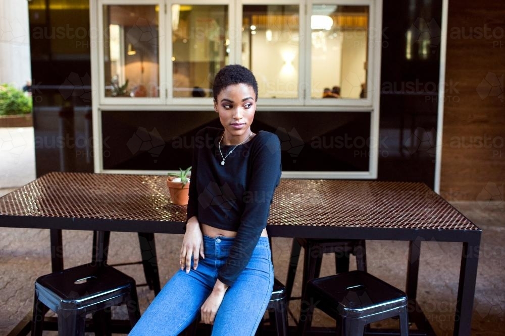 One stylish young woman sitting outside at a cafe table - Australian Stock Image