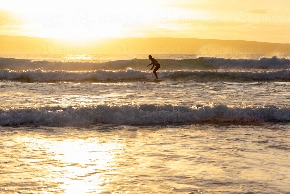 one surfer silhouetted against sunset surfing waves - Australian Stock Image