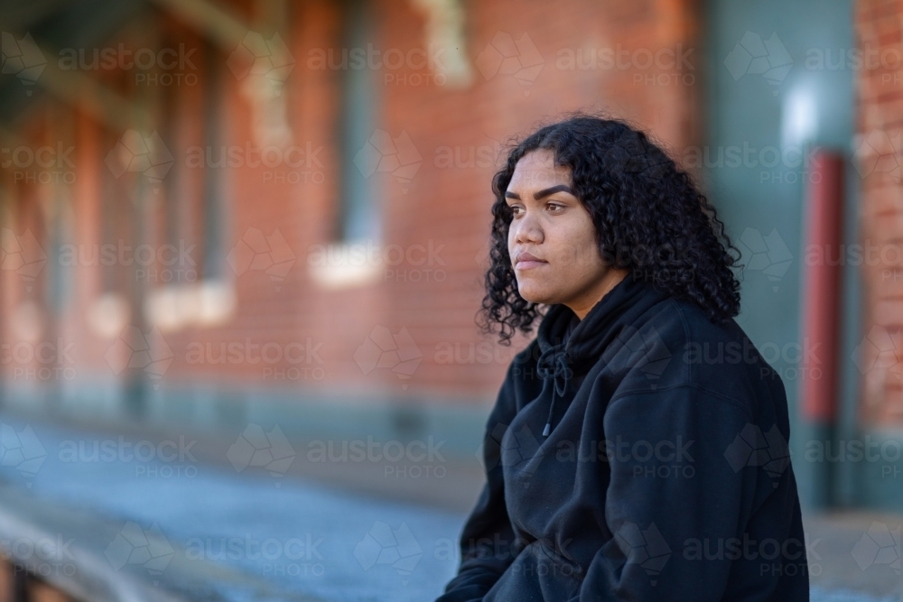one teenage girl sitting on station platform wearing black hoody - Australian Stock Image