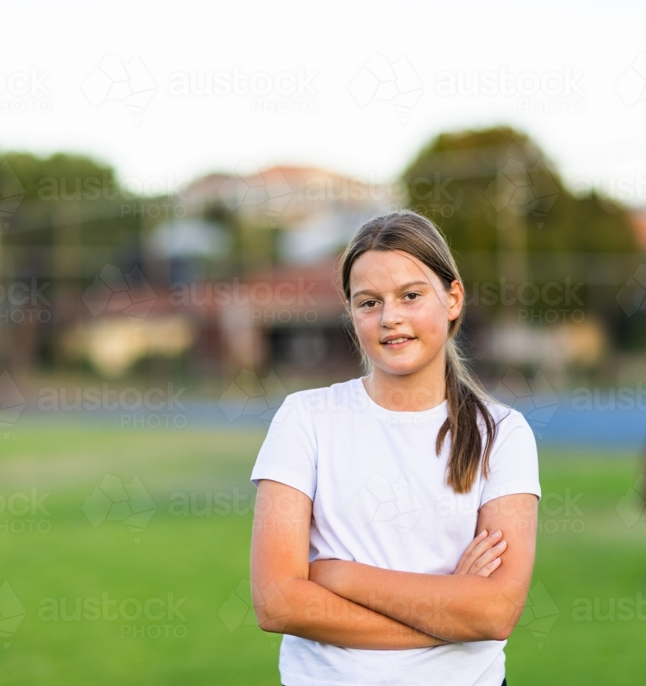 one tween girl with crossed arms wearing white tee shirt outdoors - Australian Stock Image