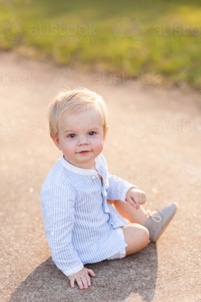 One year old boy sitting on footpath backlit by evening light - Australian Stock Image