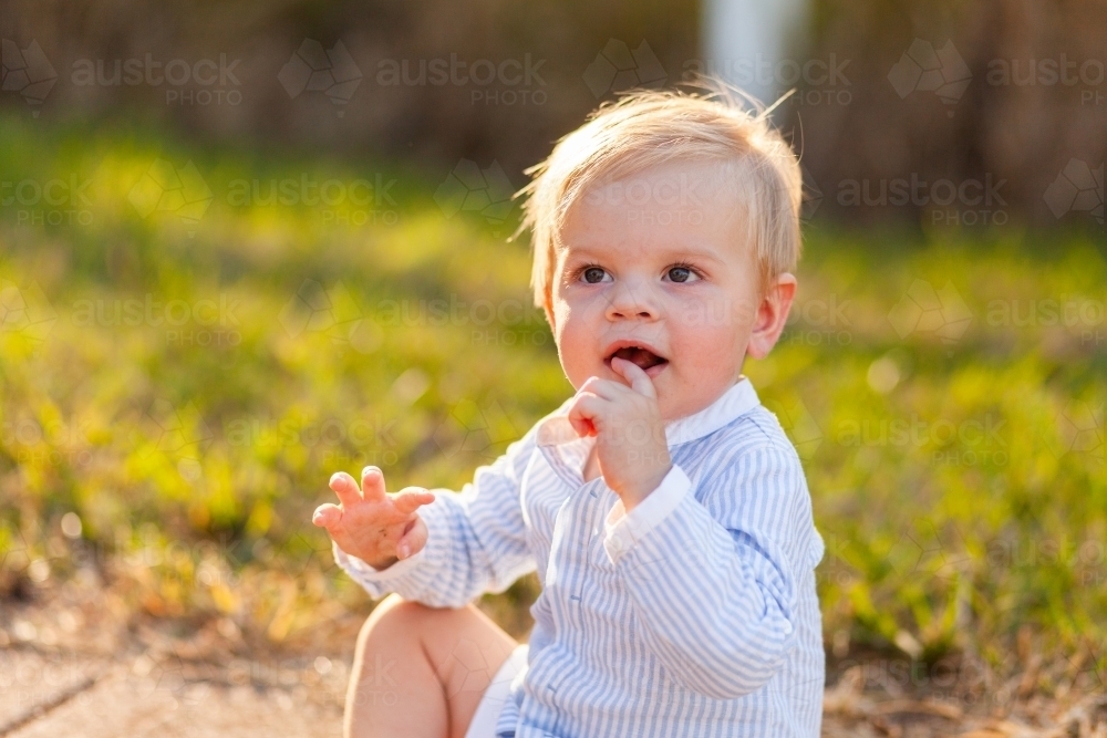 One year old boy sitting on footpath backlit by evening light - Australian Stock Image