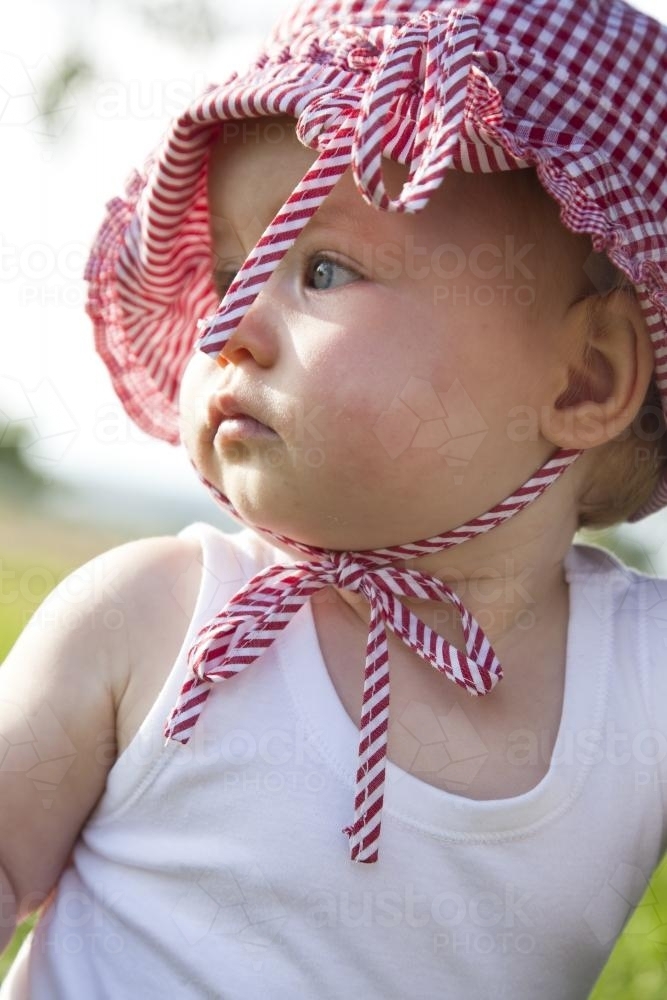 One year old girl outside wearing a red gingham sunhat - Australian Stock Image