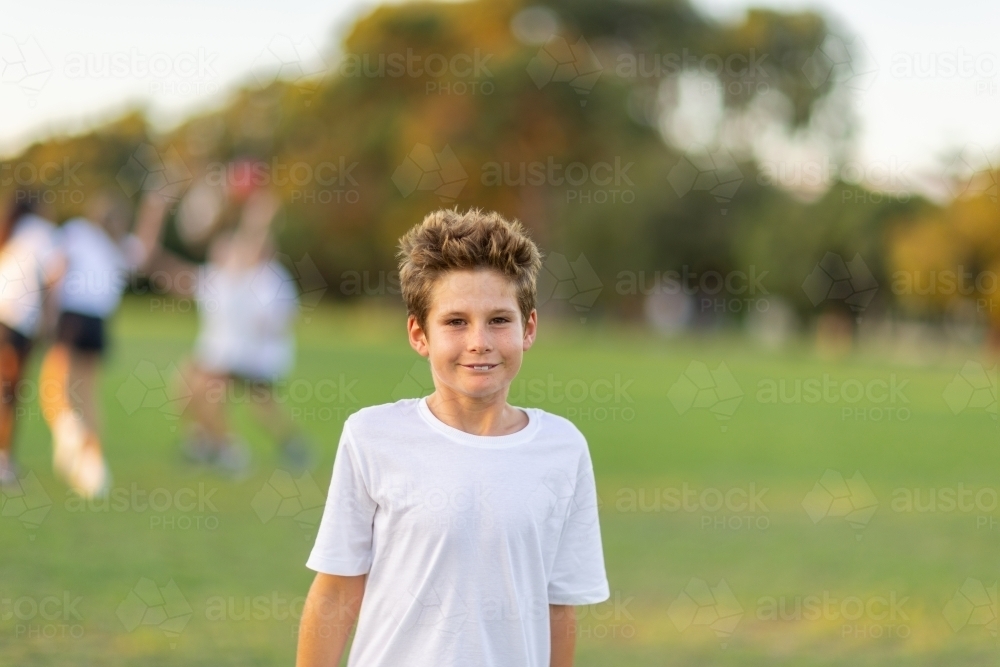 one young boy in white tee shirt with other kids out of focus playing in the background - Australian Stock Image