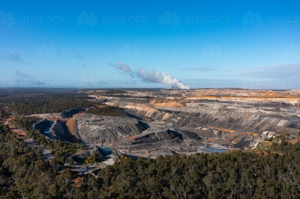 open cut coal mine surrounded by native forest, with steam from power station on horizon - Australian Stock Image