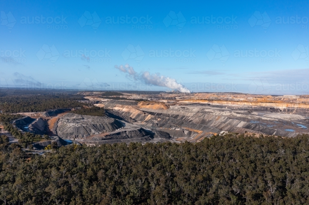 open cut coal mine with coal-fired power station on horizon and native forest in foreground - Australian Stock Image