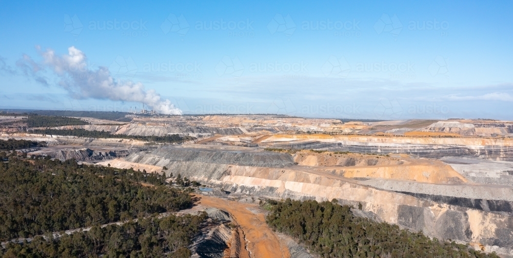 open cut coal mine with smoke from power station on horizon - Australian Stock Image