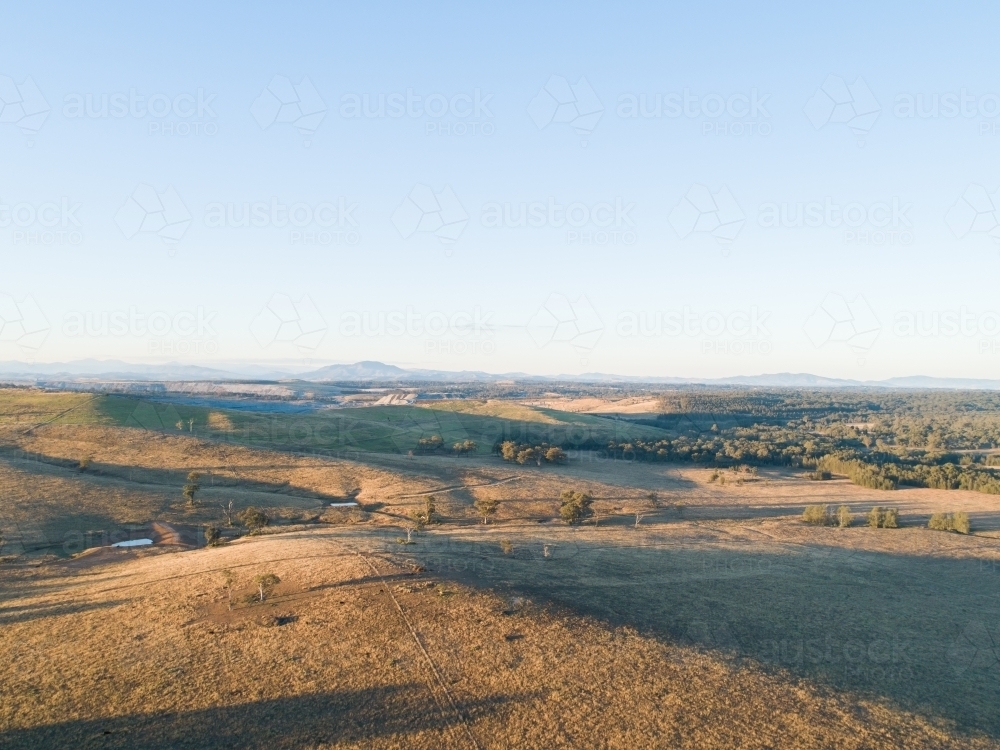 Open cut mine on horizon of farm paddock hills - Australian Stock Image