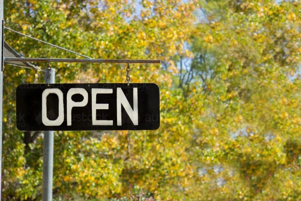 Open store sign in front of golden autumn leaves - Australian Stock Image
