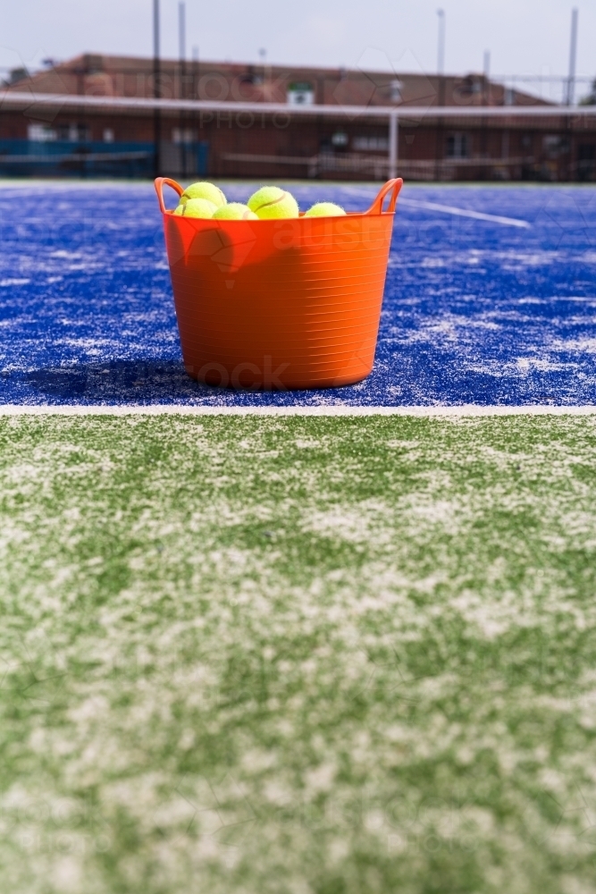 Orange basket of tennis balls on a blue and green tennis court - Australian Stock Image