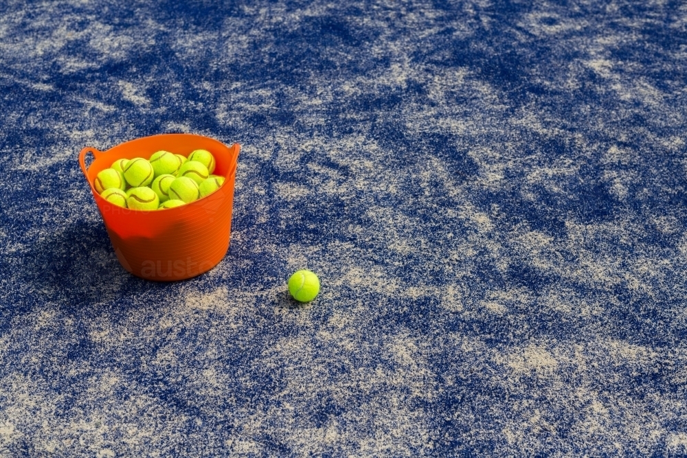Orange basket of tennis balls on a blue tennis court - Australian Stock Image