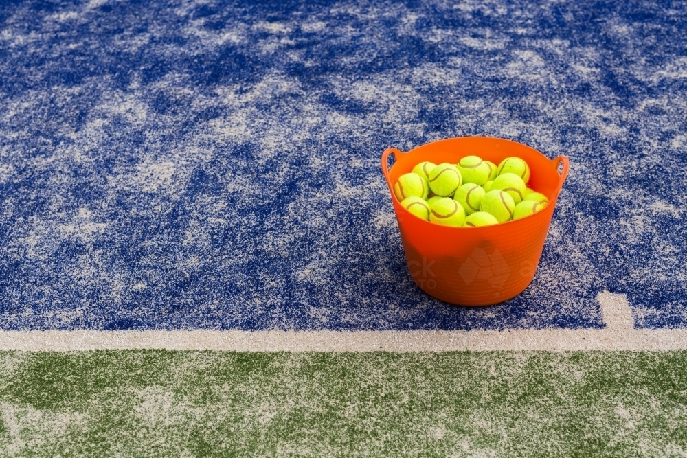 Orange basket of tennis balls on a blue tennis court - Australian Stock Image
