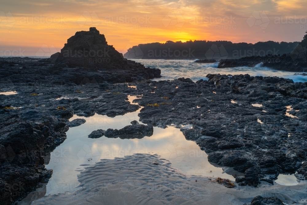 Orange clouds at dawn over rocks and ocean waves - Australian Stock Image