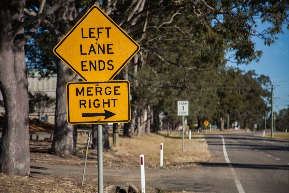 Orange left lane ends merge right sign with an arrow on the roadside - Australian Stock Image