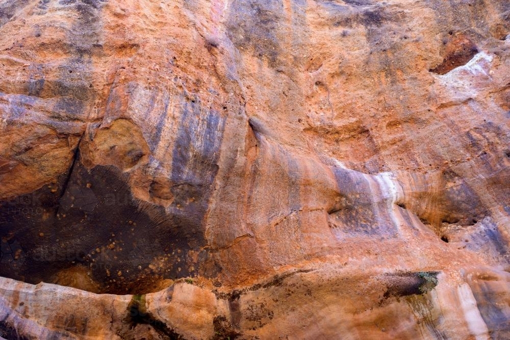 Orange rock cliff face with purple striped pattern - Australian Stock Image