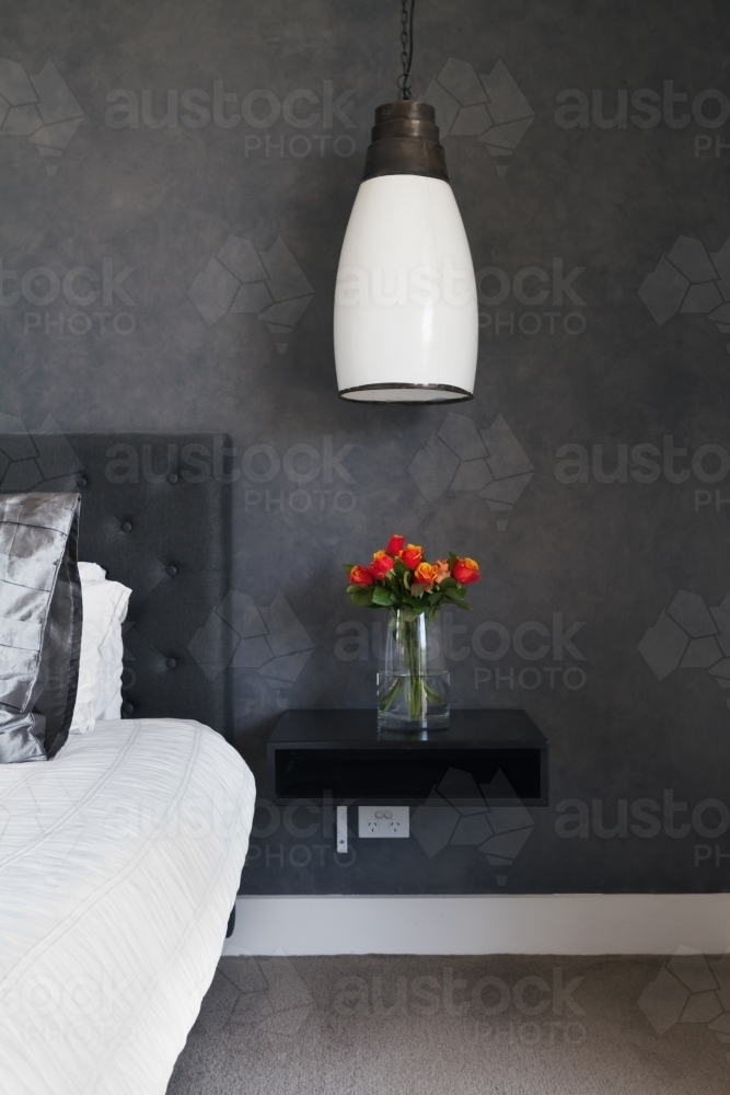 Orange roses on bedside table in contemporary dark bedroom design - Australian Stock Image