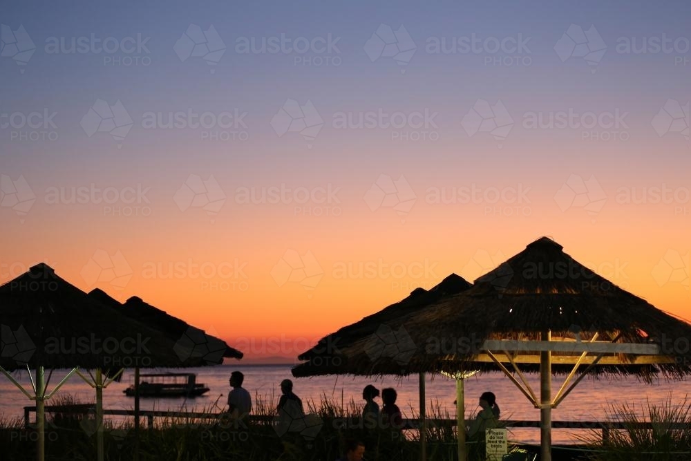 Orange sunset over thatched shelters on island - Australian Stock Image
