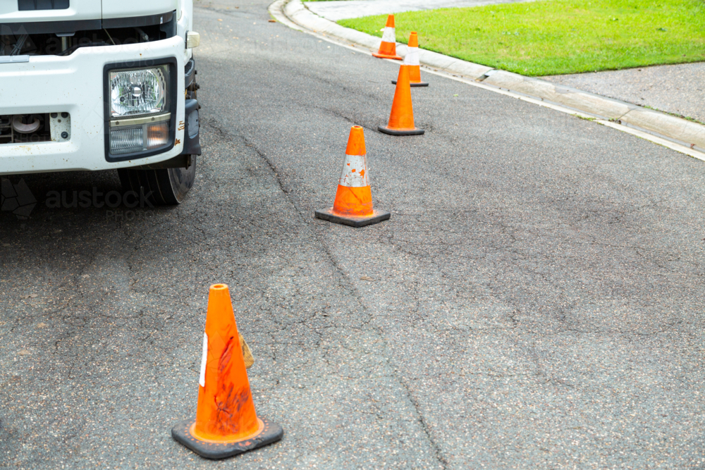 Orange traffic cones in a row blocking off work truck and suburban street. - Australian Stock Image