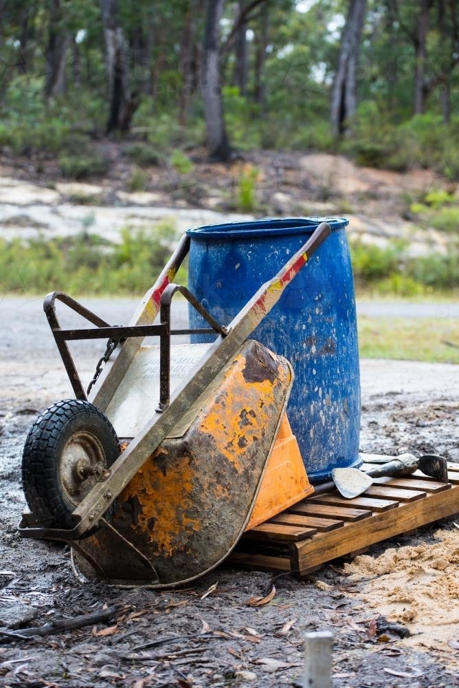 Orange wheelbarrow and blue barrel on wooden pallet - Australian Stock Image
