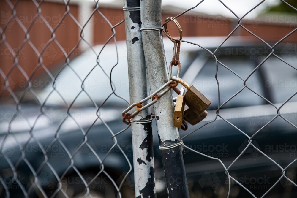 Out of focus car behind chained and padlocked fence gates - Australian Stock Image