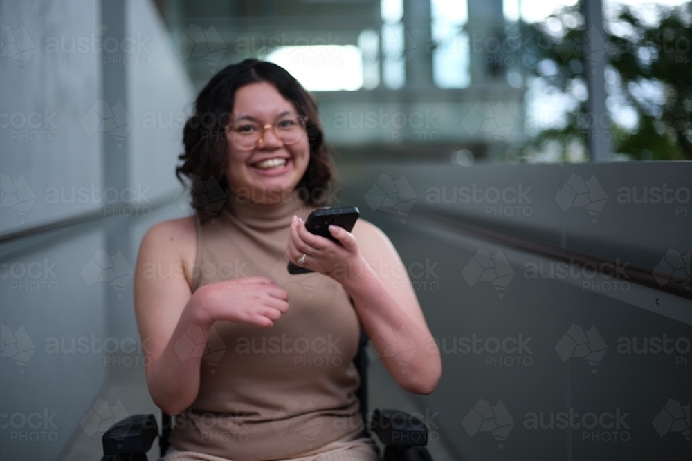 Out of focus woman with a disability sitting in a wheelchair indoors holding a mobile phone - Australian Stock Image