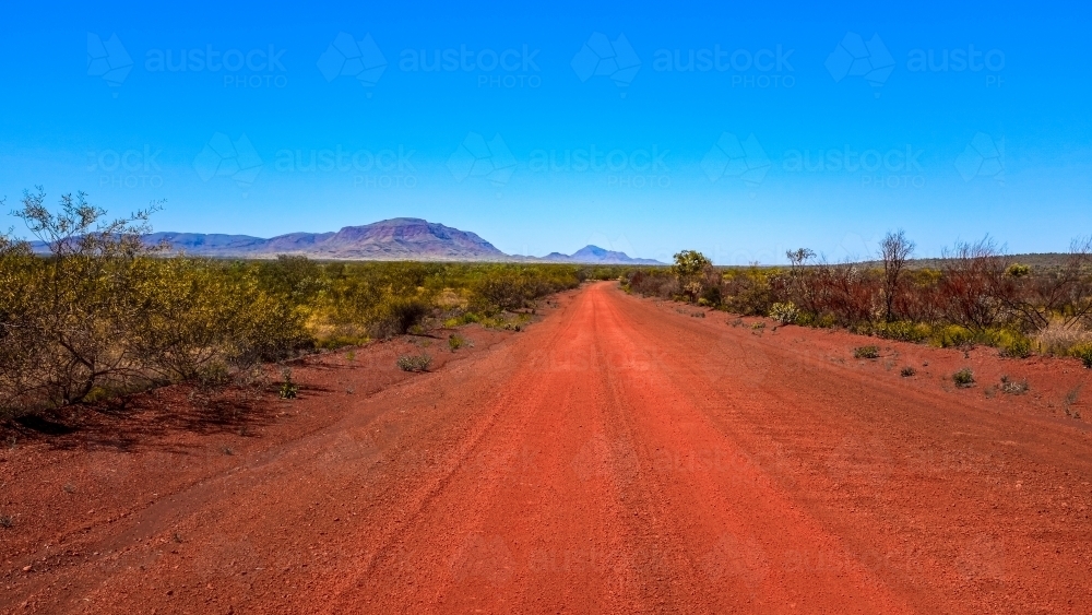 Outback red dirt road leading to mountains and blue sky - Australian Stock Image